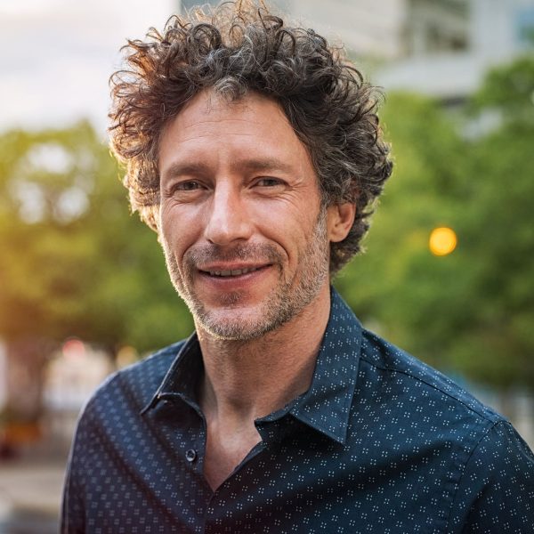 Portrait of happy mature man looking at camera outdoor. Senior businessman with beard feeling confident at sunset. Closeup face of business man smiling with city in background.
